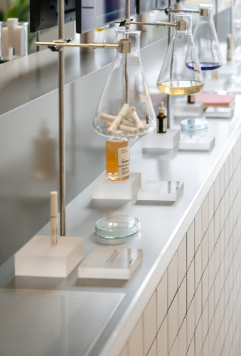 Steffi Bühlmaier Set Design. Skincare brand The Ordinary’s temporary showroom at the Highsnobiety Store in Berlin. Products are displayed in laboratory vessels on a tiled counter with steel tabletop.